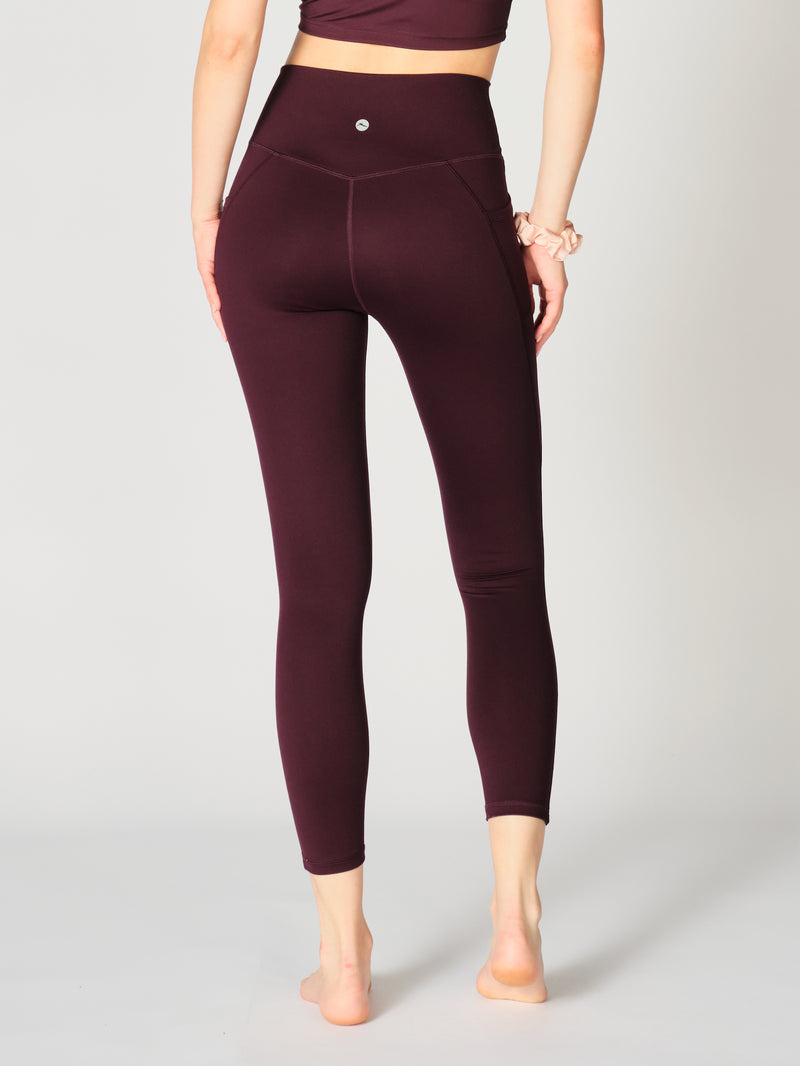 A close-up view of the X by Gottex Rachel Ankle Leggings in Merlot. The high-rise leggings emphasize her waist, and the rich merlot color presents a stylish, unified athletic look. The high-rise legging is well-suited for an active lifestyle, emphasizes her waist, and the rich merlot color presents a stylish, unified athletic look. The legging is well-suited for yoga, pilates, barre, gym, and an active lifestyle in general.