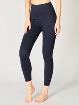 Close up view of X by Gottex Rachel ankle legging in color Midnight, that accentuate the contours of the model’s legs. An image shows the two side pockets that can fit a phone, a credit card, a set of keys, or other personal items. The design appears to be high-waisted, ankle length, tummy-control flat wide waistband, strategic placement of the seams flatter curves and elongate legs. The fabric appears to be soft, 4-way stretch, with some compression. The legging is well-suited for yoga, pilates, barre, gym
