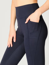 A close-up of the model featured from the waist down to the thighs, wearing X by Gottex Rachel Ankle Legging in Midnight. The leggings have a high-rise waist, providing a secure and flattering fit. On the left side, there's a conveniently placed. The fabric of the leggings appears smooth and stretchy. The merlot hue is deep and vivid, giving the leggings a versatile and stylish appeal. The legging is well-suited for yoga, pilates, barre, gym, and an active lifestyle in general.